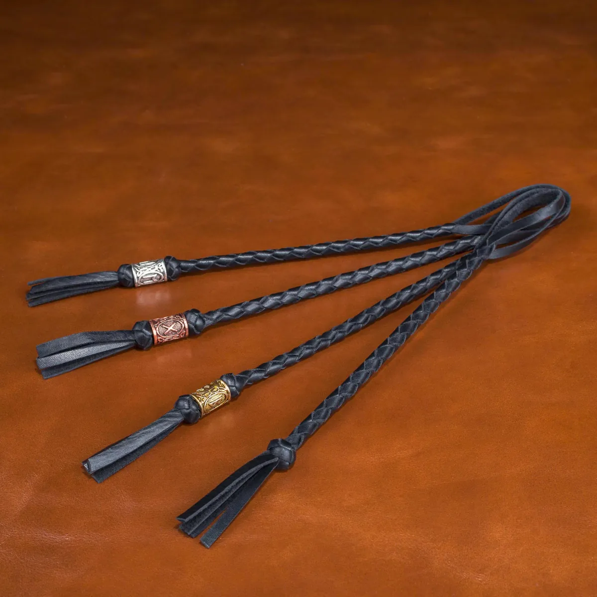 Four black braided leather knife lanyards with decorative beads and tassel finishes