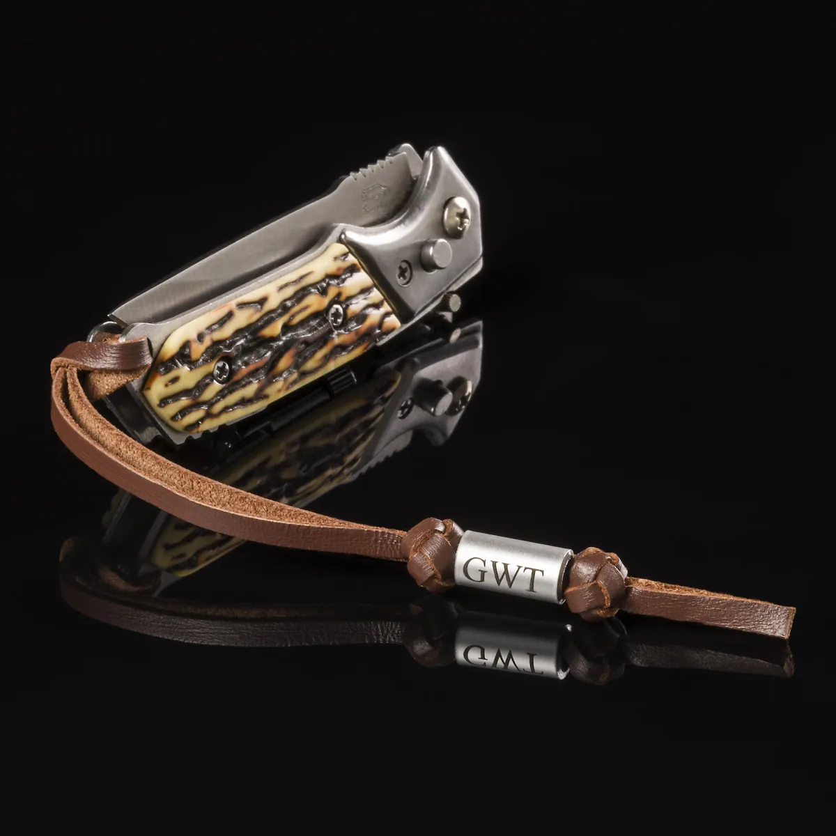 Brown leather pocket knife lanyard with personalized engraved GWT bead beside a folding knife