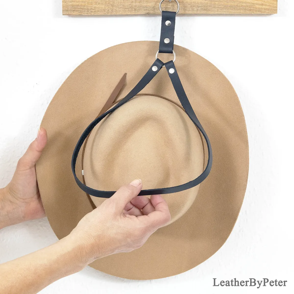 Black leather cowboy hat holder with a metal ring and rivets, shown supporting a tan cowboy hat